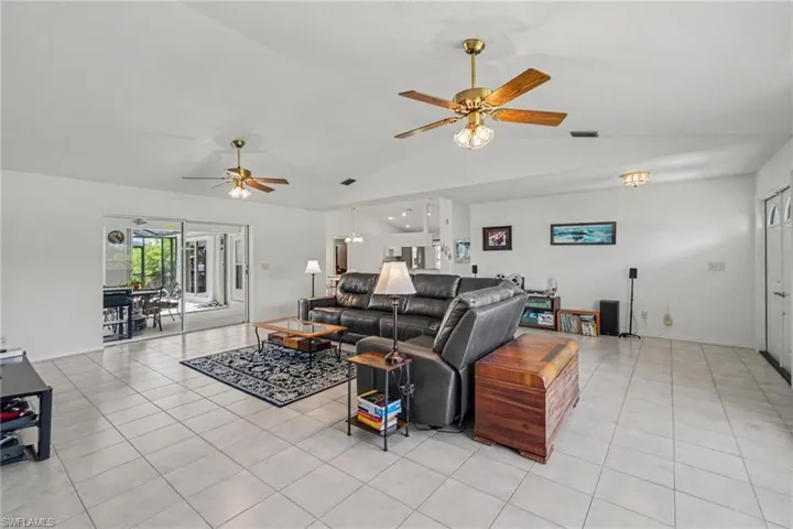 Spacious living area featuring tile flooring, vaulted ceilings, dual ceiling fans, and sliding glass doors leading to an enclosed patio