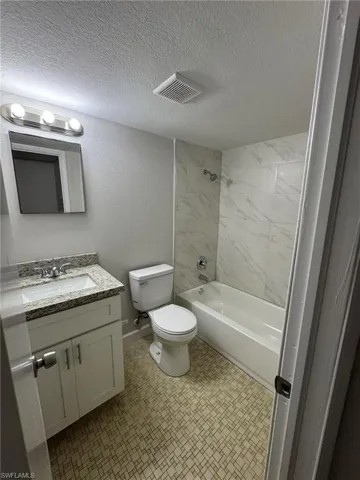 Bathroom featuring vanity, bathtub / shower combination, a textured wall, and a textured ceiling