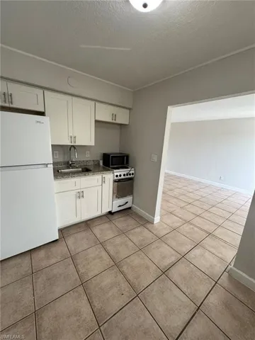 Kitchen with white cabinetry, white appliances, a textured ceiling, and light tile patterned flooring