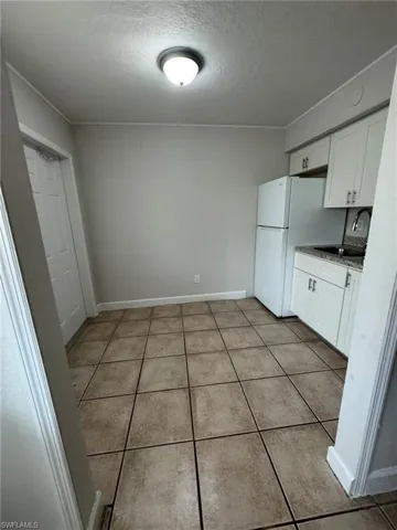 Kitchen with white cabinetry, a textured ceiling, light tile patterned flooring, and freestanding refrigerator
