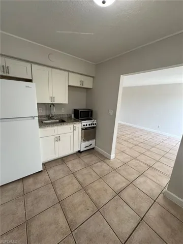 Kitchen with white appliances, white cabinetry, a textured ceiling, and light tile patterned floors