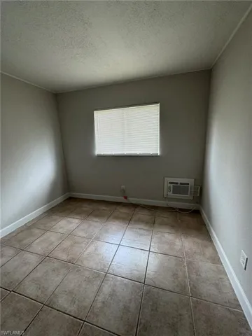 Unfurnished room with a textured ceiling, light tile patterned floors, and an AC wall unit