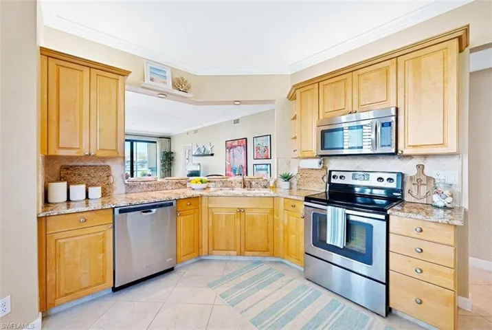 Kitchen featuring stainless steel appliances, crown molding, tasteful backsplash, light stone counters, and light tile patterned floors