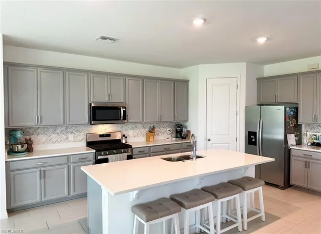 Kitchen featuring a kitchen island with sink, gray cabinetry, a breakfast bar, and appliances with stainless steel finishes