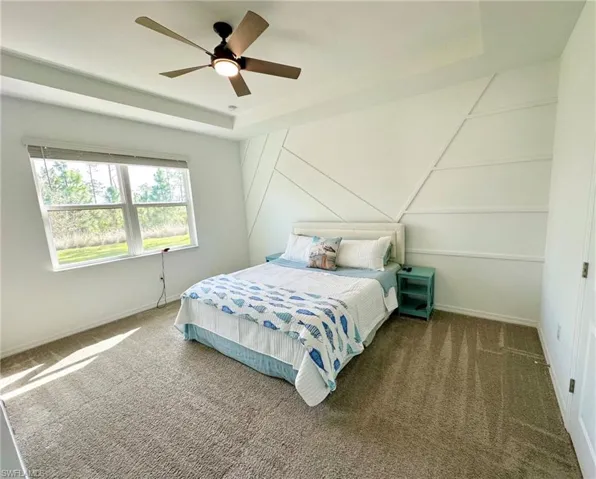 Carpeted bedroom featuring a tray ceiling and ceiling fan
