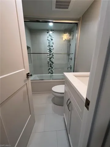 Bathroom featuring tile patterned flooring, visible vents, toilet, enclosed tub / shower combo, and vanity