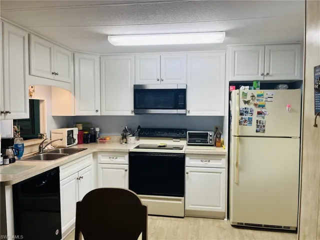 Kitchen with range with electric cooktop, stainless steel microwave, white cabinets, freestanding refrigerator, and light wood-style floors