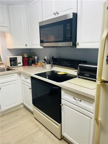 Kitchen featuring white appliances, white cabinets, light countertops, and light wood finished floors