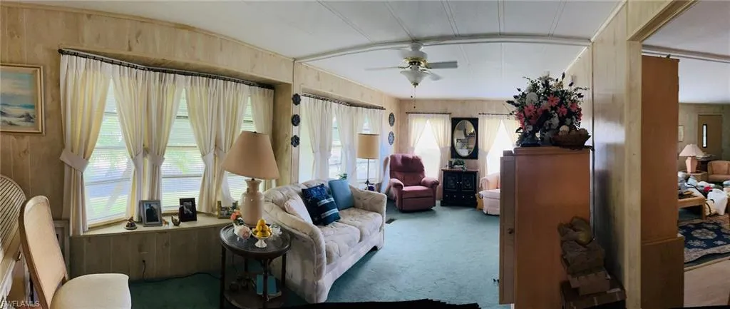 Carpeted living room with ceiling fan and wooden walls