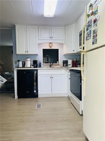 Kitchen featuring appliances, white cabinets, light countertops, and light wood finished floors