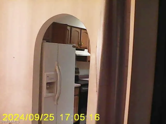 Kitchen view of white fridge with ice dispenser, arched walkways, range, light countertops, and dark wood finish cabinets