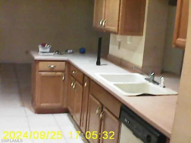 Kitchen with light countertops, wood finish cabinets, light tile patterned flooring, and dishwasher