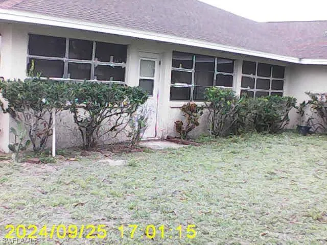 View of property exterior with stucco siding, a yard, and a shingled roof