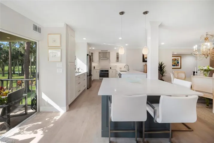 Kitchen featuring light hardwood / wood-style flooring, stainless steel appliances, a notable chandelier, wall chimney range hood, and white cabinetry