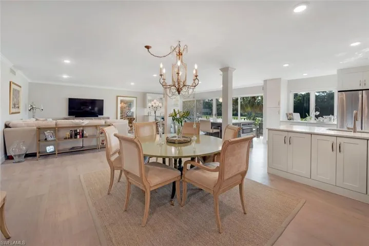 Dining area featuring ornamental molding, decorative columns, light wood-type flooring, a notable chandelier, and sink
