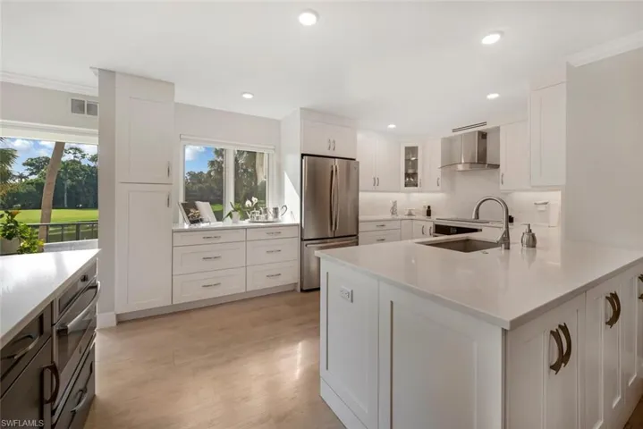 Kitchen featuring light hardwood / wood-style floors, crown molding, wall chimney range hood, white cabinets, and stainless steel refrigerator