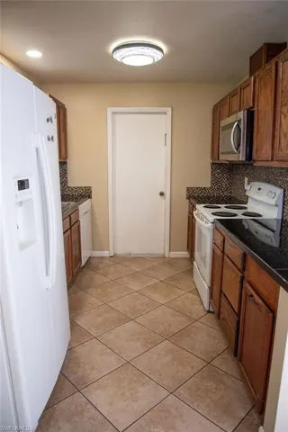 Kitchen featuring white fridge with ice dispenser, ceiling fan, dark countertops, light tile patterned flooring, and french doors