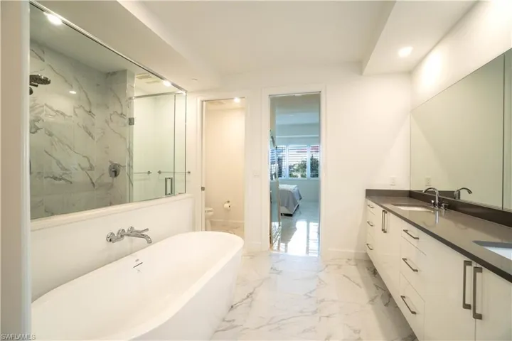 Ensuite bathroom with double vanity, a marble finish shower, light marble finish flooring, recessed lighting, and a freestanding tub
