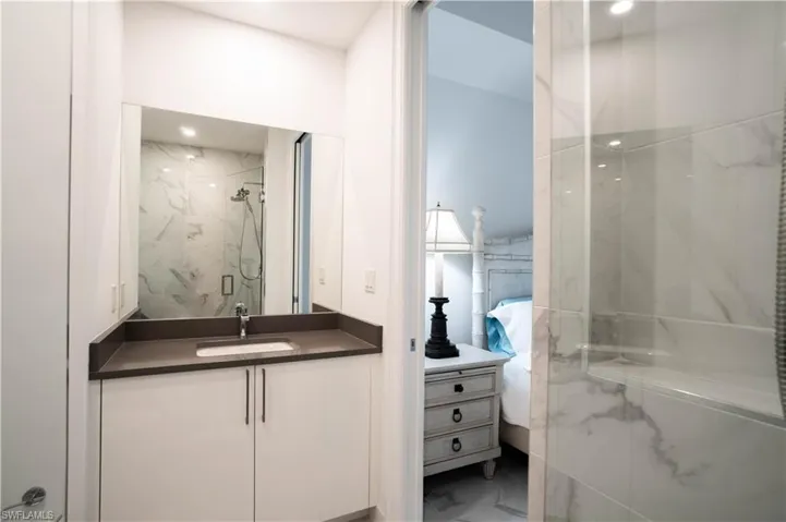 Ensuite bathroom featuring vanity, a marble finish shower, and marble look tiles
