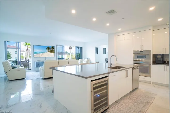 Kitchen featuring open floor plan, white cabinets, an island with sink, beverage cooler, and recessed lighting