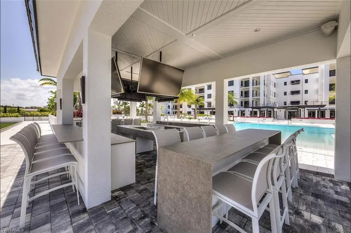 Covered outdoor entertaining area featuring multiple built-in bars with stone-finish countertops, overhead ceiling fans, built-in televisions, and textured paver flooring