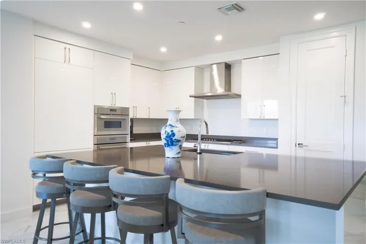 Contemporary kitchen featuring a large central island with seating, high-gloss white cabinetry, stainless steel appliances, and recessed lighting
