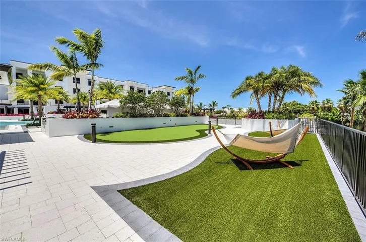 Outdoor amenity space featuring paver stone hardscaping, artificial turf lawn, and mature palm trees