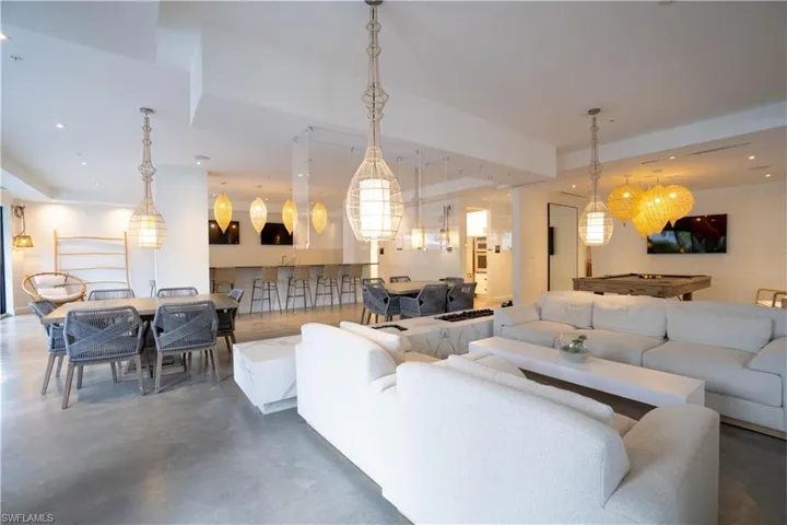 Spacious entertainment area featuring concrete flooring, a built-in wet bar with seating, multiple pendant light fixtures, and a shiplap accent wall