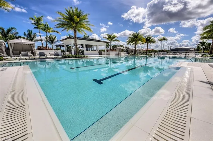Resort-style pool area featuring a lap lane, surrounding lounge areas, a poolside cabana with seating, and tropical palm tree landscaping