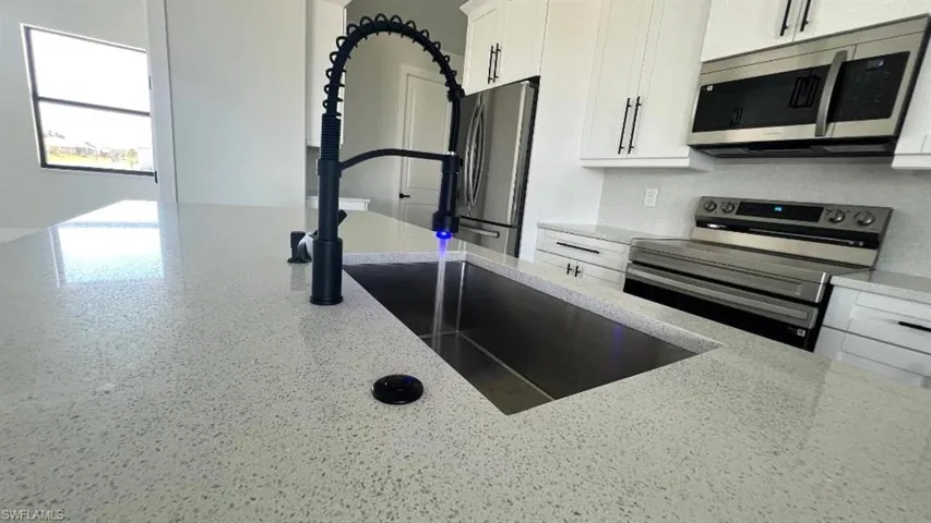 Kitchen featuring light stone countertops, appliances with stainless steel finishes, white cabinetry, a sink, and backsplash