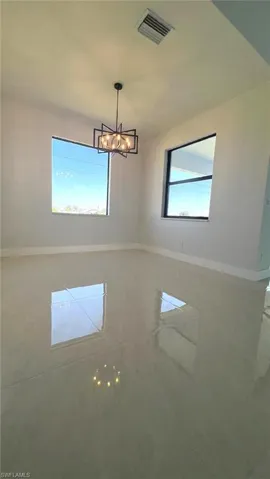 Unfurnished room featuring baseboards, visible vents, and a chandelier