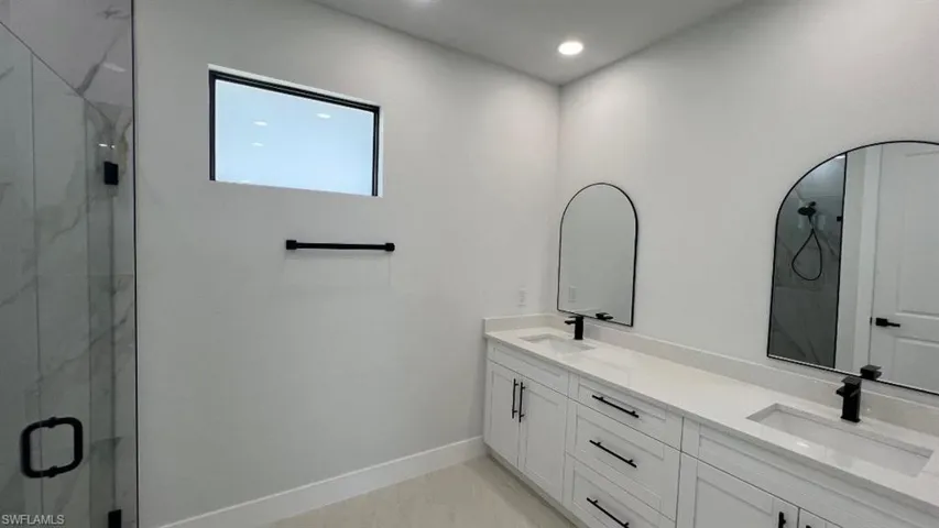 Full bath with double vanity, a sink, a marble finish shower, and baseboards