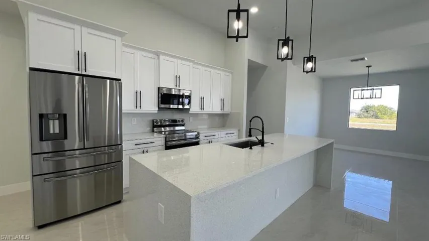 Kitchen with backsplash, a sink, white cabinets, a kitchen island with sink, and appliances with stainless steel finishes