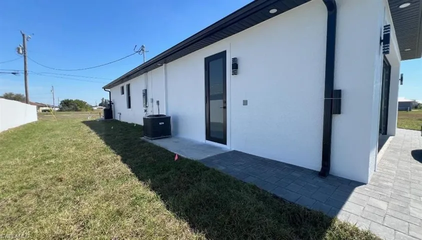 View of side of property featuring central AC unit, stucco siding, and a lawn