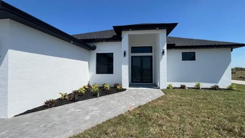 Entrance to property with a yard, stucco siding, french doors, and roof with shingles