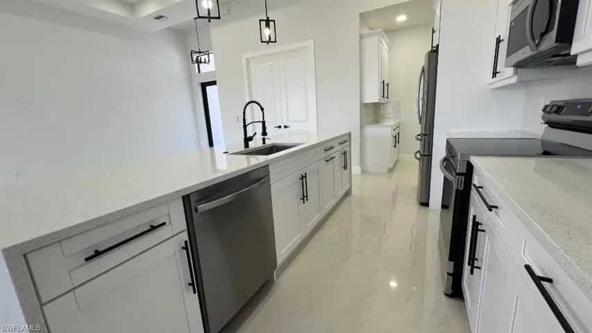 Kitchen with light stone counters, a sink, white cabinetry, appliances with stainless steel finishes, and hanging light fixtures
