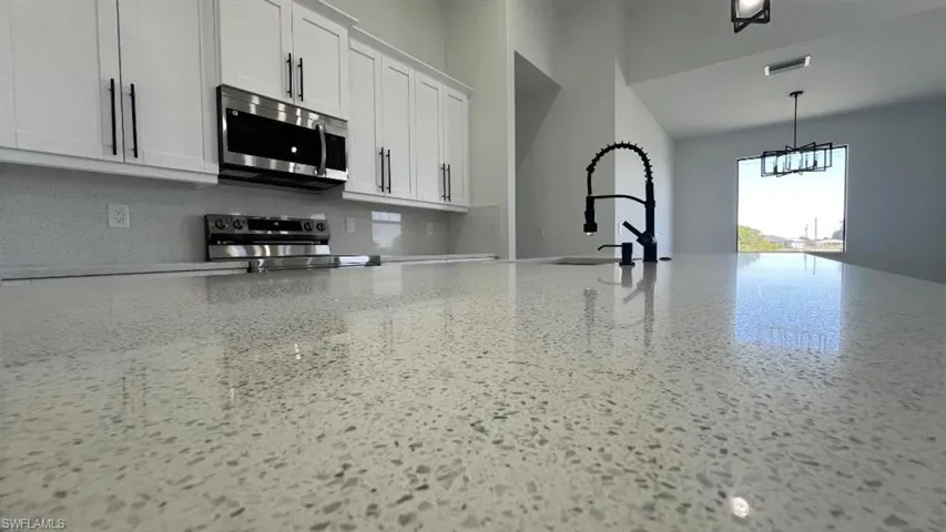 Kitchen with speckled floor, a sink, light stone countertops, stainless steel appliances, and visible vents
