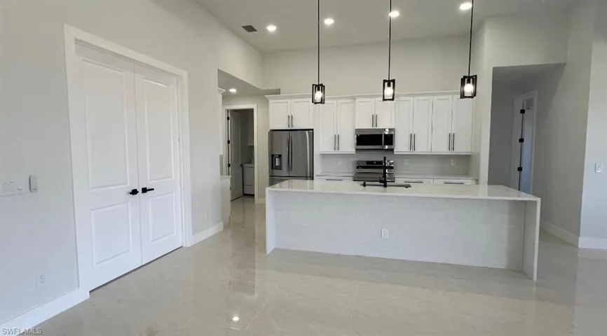 Kitchen with white cabinets, visible vents, appliances with stainless steel finishes, an island with sink, and a high ceiling