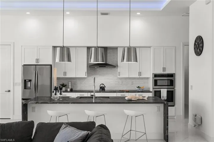 Kitchen featuring white cabinets, stainless steel appliances, dark stone countertops, a breakfast bar area, and decorative light fixtures