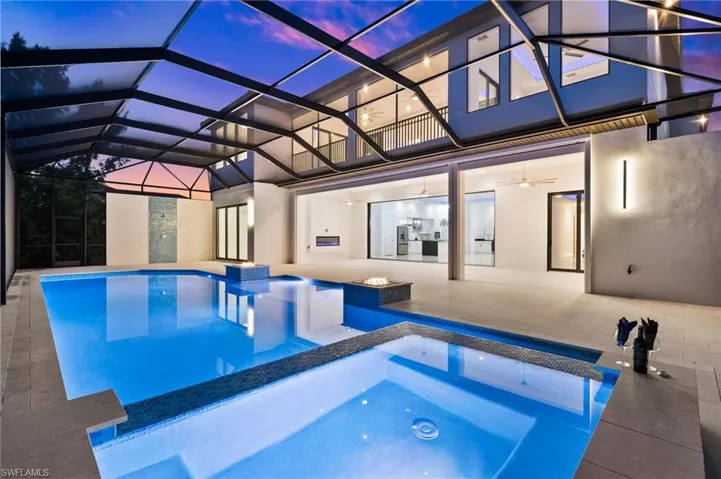 Pool at dusk with a pool with connected hot tub, a lanai, and a patio