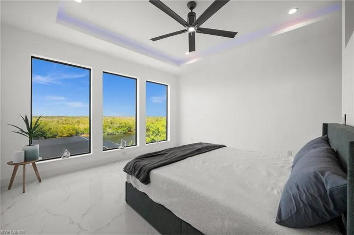 Bedroom featuring a raised ceiling, marble finish flooring, a ceiling fan, recessed lighting, and a water view