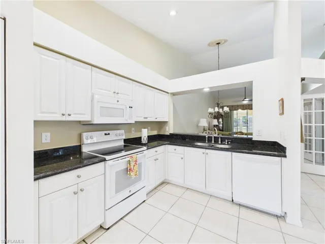 Kitchen featuring white appliances, light tile patterned floors, white cabinets, dark stone countertops, and a sink