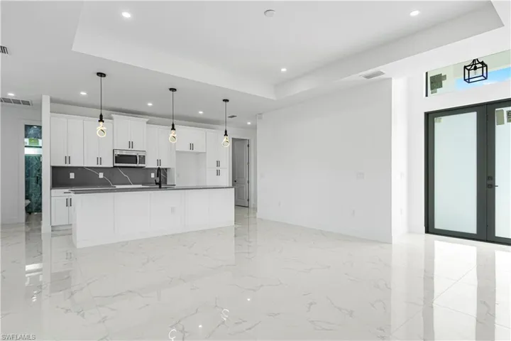 Kitchen with white cabinetry, sink, tasteful backsplash, a tray ceiling, and a kitchen island with sink