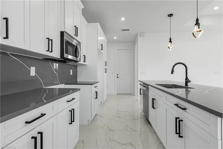 Kitchen with appliances with stainless steel finishes, decorative light fixtures, sink, and dark stone counters