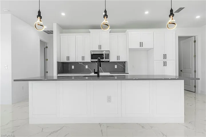 Kitchen featuring pendant lighting, white cabinetry, and an island with sink