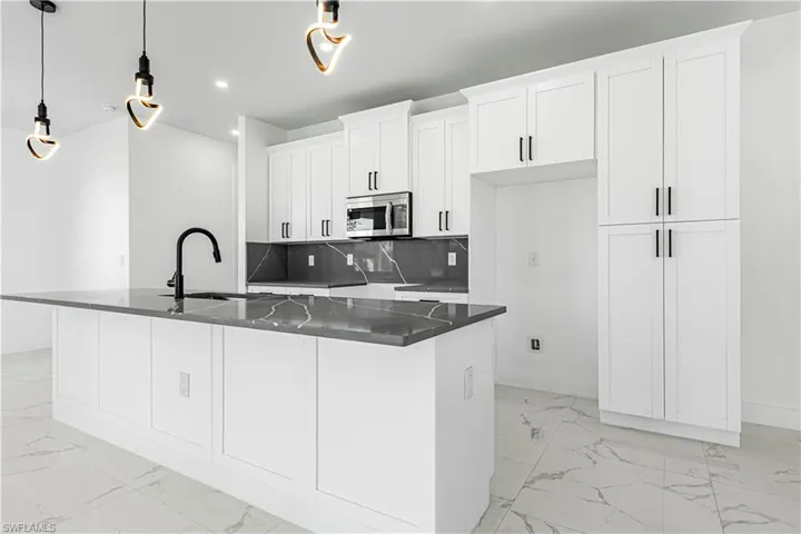 Kitchen with backsplash, white cabinets, a kitchen island with sink, and hanging light fixtures