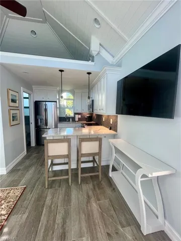 Kitchen with stainless steel refrigerator with ice dispenser, hanging light fixtures, white cabinets, dark wood finished floors, and a peninsula