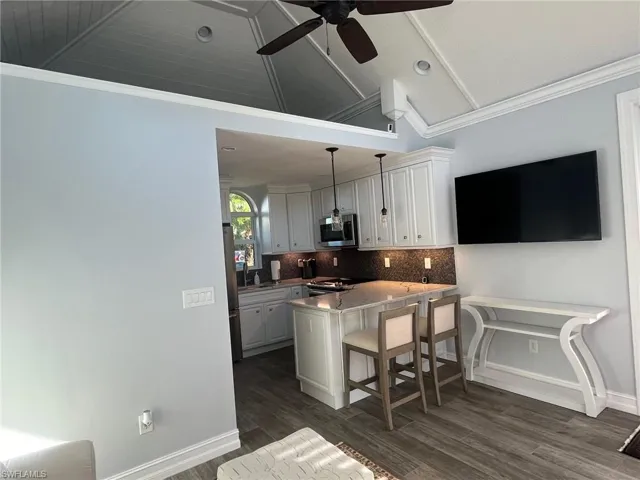 Kitchen with crown molding, pendant lighting, a kitchen breakfast bar, white cabinetry, and a peninsula