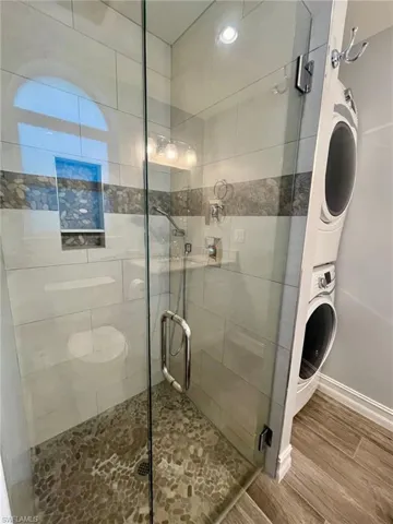 Bathroom with a stall shower, wood finish floors, and estacked washer and dryer
