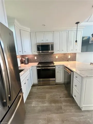 Kitchen with appliances with stainless steel finishes, white cabinets, light stone countertops, decorative light fixtures, and backsplash